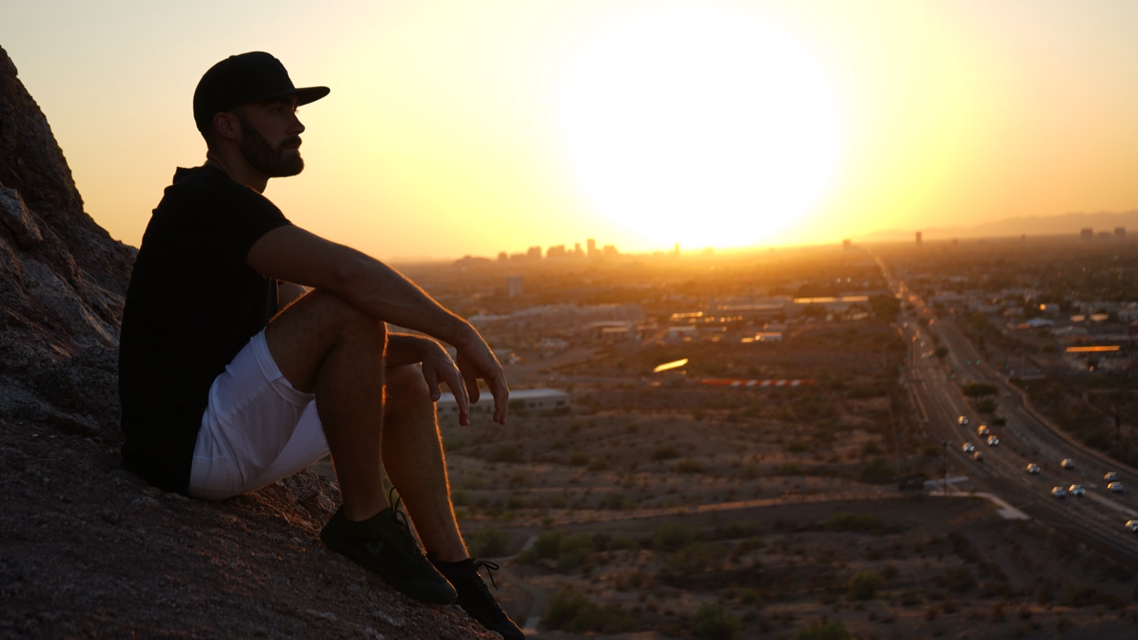 Ryan McBurney on a Papago Park butte at sunset, hand resting on his knee, the Phoenix skyline and horizon glowing behind him